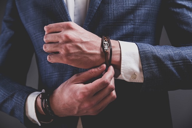 Fashion portrait of young businessman handsome model man dressed in elegant blue suit with accessories on hands posing on gray background in studio Fashion portrait of young businessman handsome model man dressed in elegant blue suit with accessories on hands posing on gray background in studio
