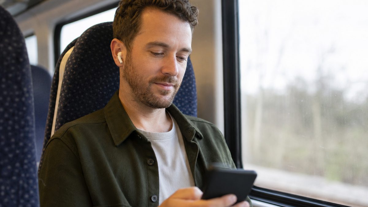 Person wearing compact wireless earbuds while commuting on a UK train