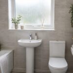 Small UK rented bathroom with a freestanding ladder shelf holding folded towels and a basket beside a pedestal sink