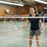 Adult beginner holding a badminton racket on an indoor court ready to play
